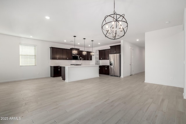 kitchen with hanging light fixtures, a center island with sink, stainless steel fridge, and light wood-type flooring