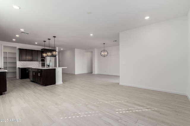 kitchen with a kitchen island with sink, backsplash, stainless steel refrigerator with ice dispenser, a notable chandelier, and decorative light fixtures