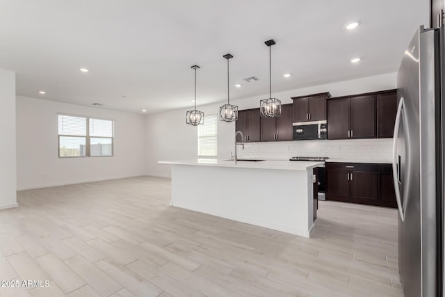 kitchen featuring decorative light fixtures, sink, dark brown cabinetry, stainless steel appliances, and a center island with sink