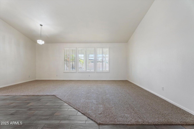 spare room featuring a chandelier, dark carpet, and lofted ceiling