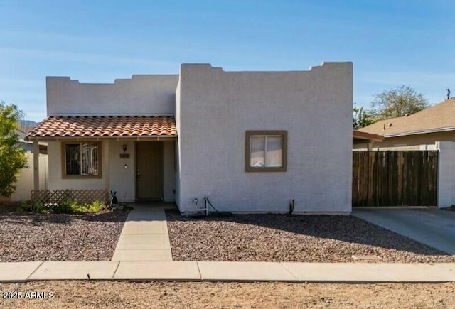 view of front facade featuring a tiled roof, fence, concrete driveway, and stucco siding