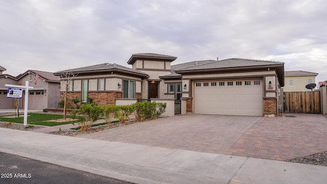 prairie-style house featuring decorative driveway, brick siding, fence, and an attached garage