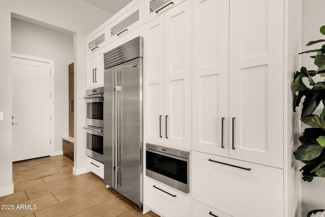 kitchen with white cabinetry, glass insert cabinets, baseboards, and built in appliances