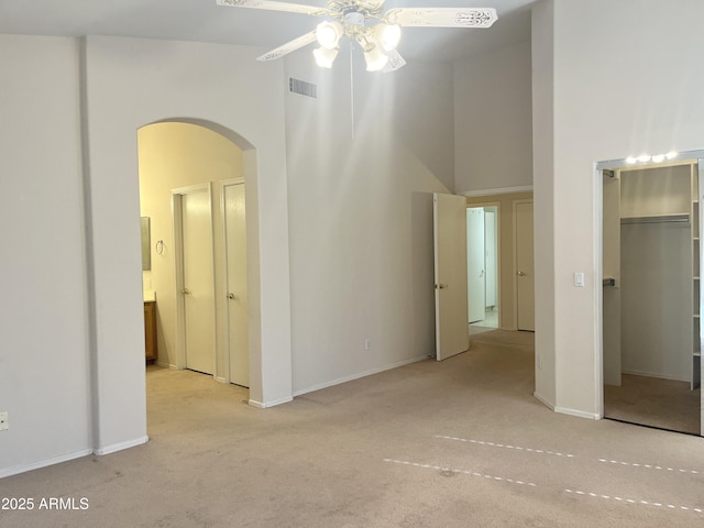 spare room featuring a towering ceiling, light colored carpet, and ceiling fan