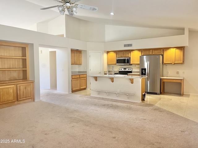 kitchen featuring a kitchen bar, stainless steel appliances, light colored carpet, a kitchen island with sink, and high vaulted ceiling