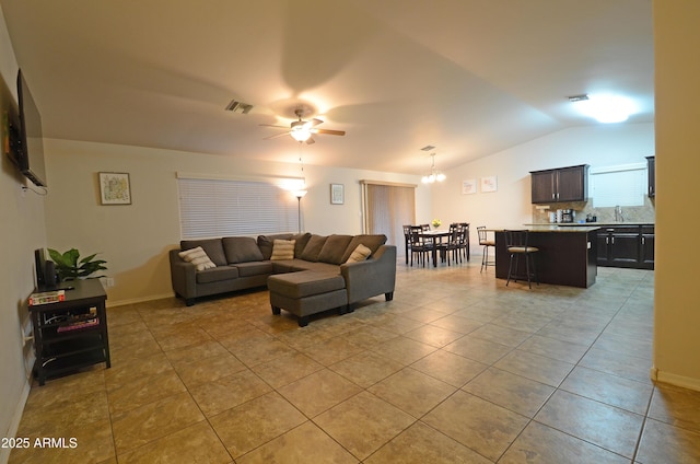 living room with visible vents, ceiling fan with notable chandelier, light tile patterned floors, baseboards, and vaulted ceiling