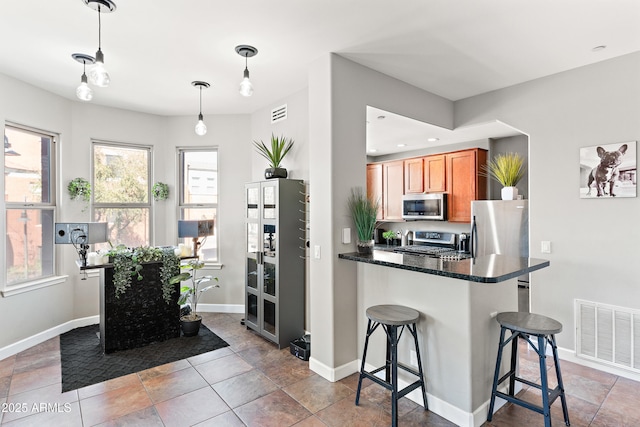 kitchen with visible vents, dark countertops, appliances with stainless steel finishes, a breakfast bar area, and brown cabinetry