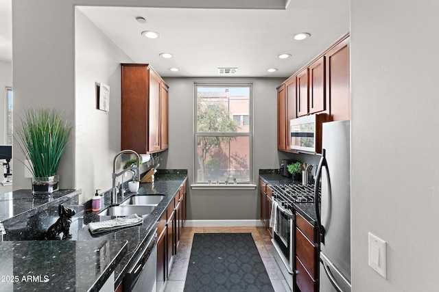 kitchen with visible vents, a sink, dark stone countertops, appliances with stainless steel finishes, and baseboards