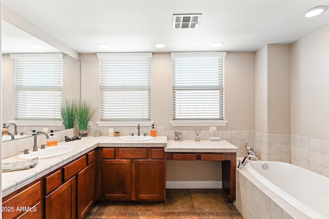 full bath featuring a garden tub, double vanity, visible vents, and a sink