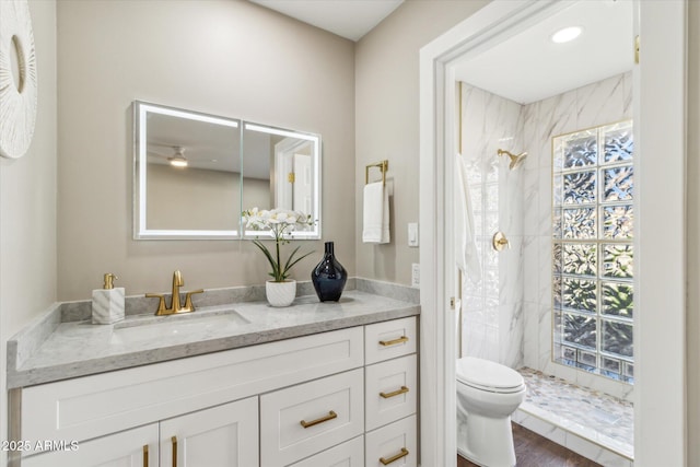 bathroom with toilet, hardwood / wood-style flooring, tiled shower, ceiling fan, and vanity