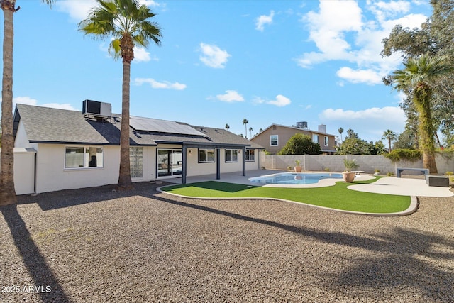 rear view of house with a patio, cooling unit, a fenced in pool, and solar panels