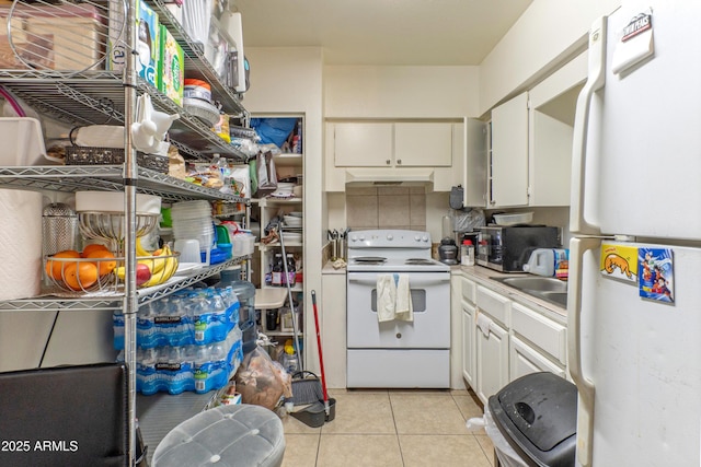 kitchen featuring light tile patterned floors, white cabinetry, a sink, white appliances, and under cabinet range hood