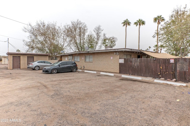 single story home featuring uncovered parking, fence, an outdoor structure, and brick siding