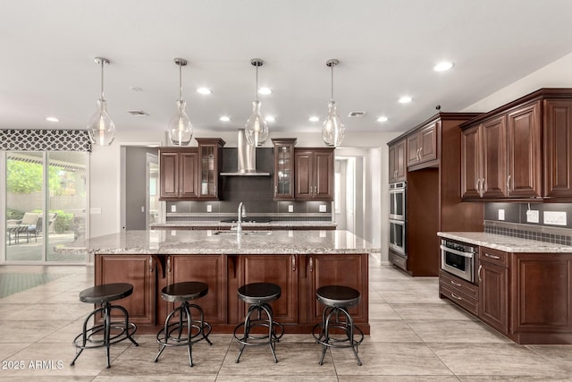 kitchen featuring visible vents, tasteful backsplash, a breakfast bar, stainless steel appliances, and wall chimney exhaust hood