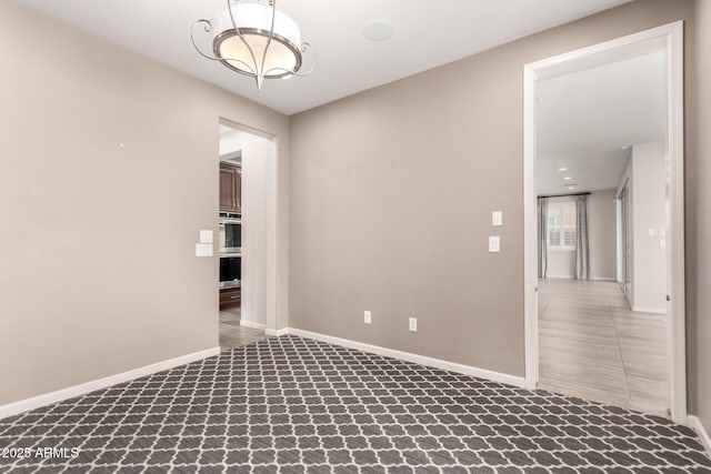 carpeted empty room with baseboards and a notable chandelier