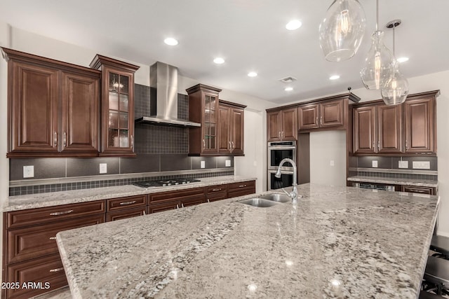 kitchen featuring decorative backsplash, wall chimney range hood, a large island with sink, a sink, and stainless steel appliances