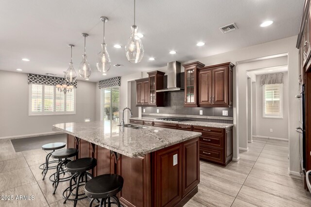 kitchen featuring a sink, a kitchen breakfast bar, wall chimney exhaust hood, baseboards, and cooktop