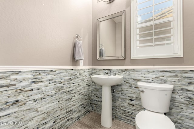 bathroom featuring tile walls, wainscoting, and toilet