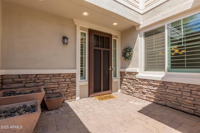 doorway to property featuring a patio, stucco siding, and stone siding