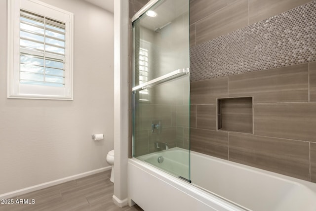 bathroom featuring baseboards, shower / bath combination with glass door, wood finished floors, and toilet