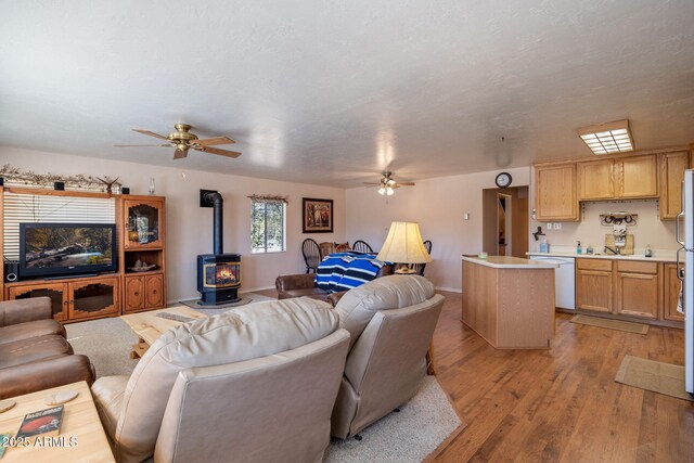 living area with light wood finished floors, baseboards, a wood stove, and a ceiling fan