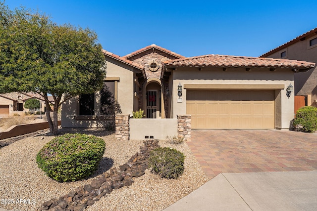 mediterranean / spanish house with an attached garage, stone siding, a tiled roof, decorative driveway, and stucco siding