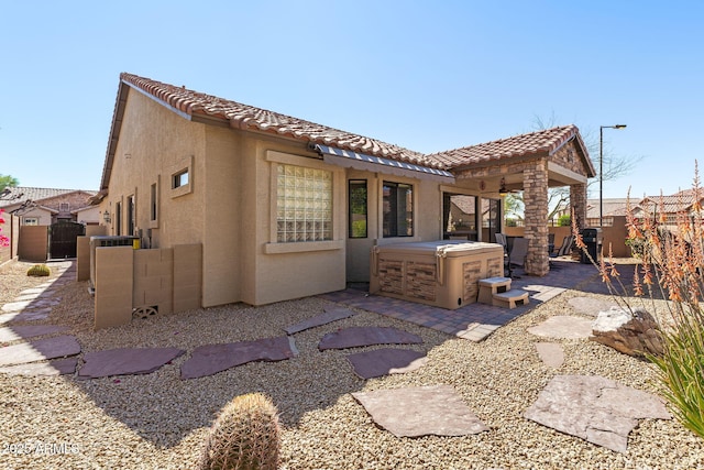 back of property with fence, a tile roof, stucco siding, a patio area, and a hot tub