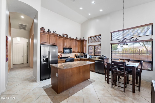 kitchen featuring arched walkways, brown cabinets, visible vents, a kitchen island, and black appliances