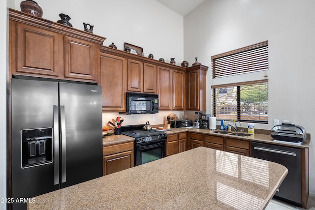 kitchen with brown cabinets, a high ceiling, light countertops, black appliances, and a sink