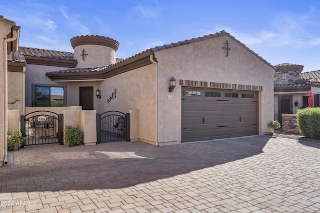 mediterranean / spanish-style home with an attached garage, a tile roof, a gate, and stucco siding