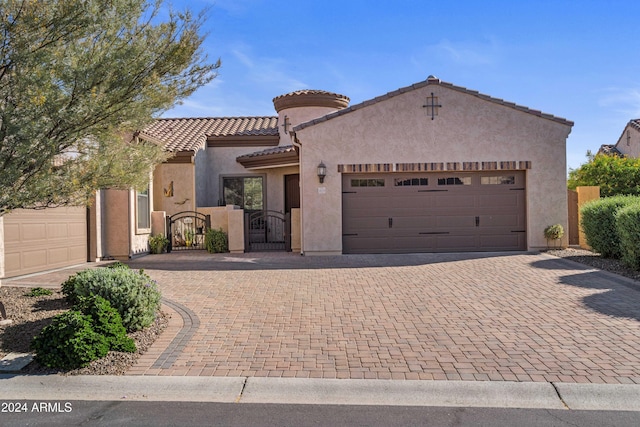 mediterranean / spanish-style house with an attached garage, a tile roof, decorative driveway, a gate, and stucco siding