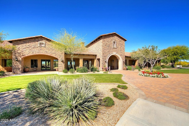 mediterranean / spanish house featuring stone siding, a front yard, and stucco siding