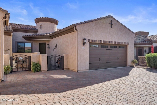 mediterranean / spanish-style house with an attached garage, a tiled roof, a gate, and stucco siding