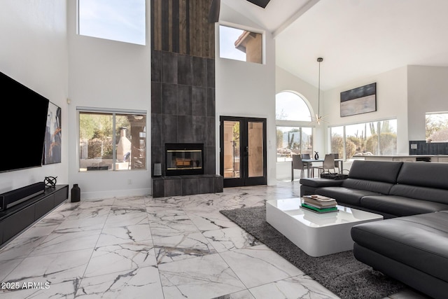 living room featuring a tiled fireplace, a high ceiling, a healthy amount of sunlight, and french doors