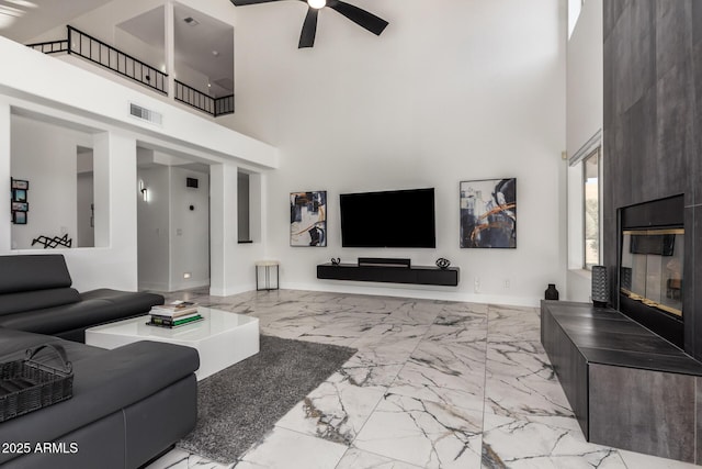 living room featuring ceiling fan, a fireplace, and a high ceiling