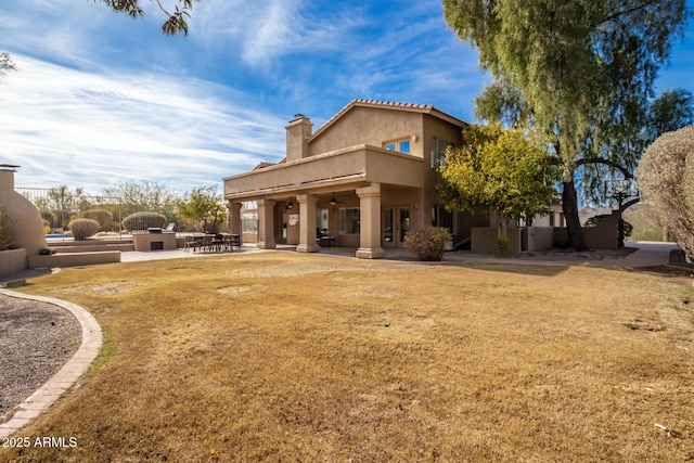 rear view of property featuring ceiling fan, a balcony, a patio area, and a lawn