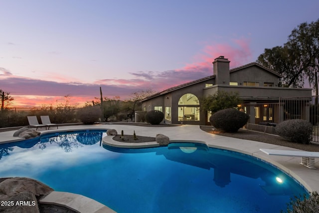 pool at dusk with a diving board and a patio