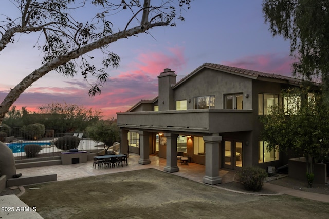 back house at dusk featuring a fenced in pool and a patio