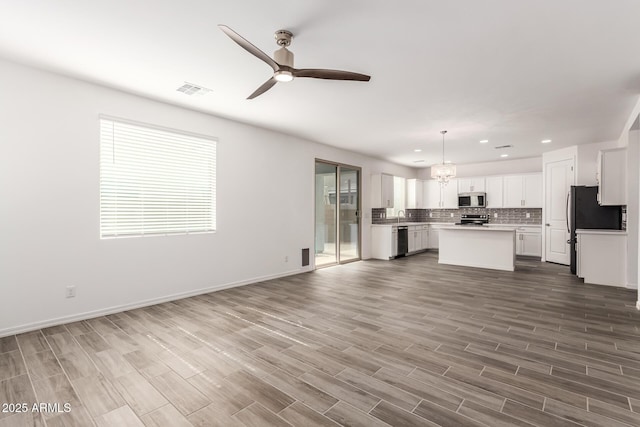 kitchen with white cabinetry, backsplash, stainless steel appliances, a kitchen island, and decorative light fixtures