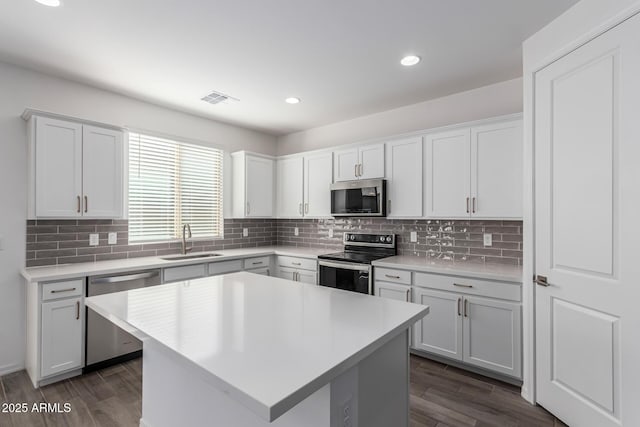 kitchen with sink, tasteful backsplash, a kitchen island, stainless steel appliances, and white cabinets