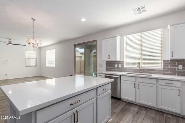 kitchen with sink, stainless steel dishwasher, a kitchen island, pendant lighting, and decorative backsplash