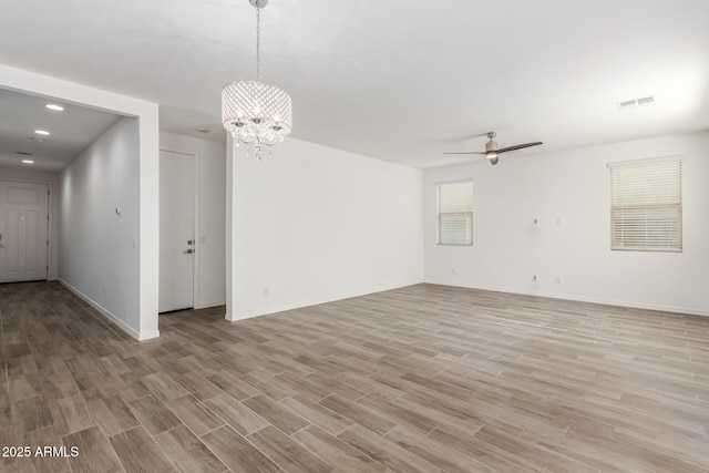 empty room with ceiling fan with notable chandelier and light hardwood / wood-style flooring