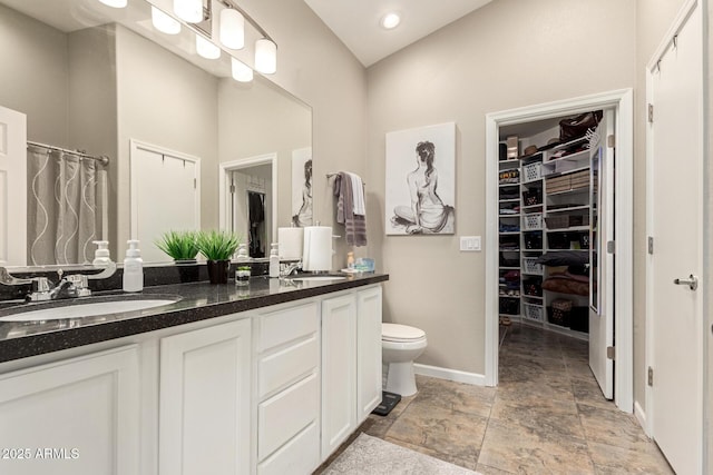 bathroom with a walk in closet, double vanity, toilet, and a sink