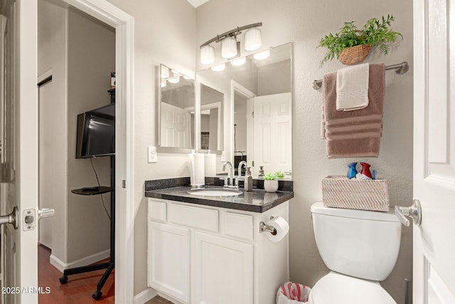 bathroom featuring baseboards, toilet, wood finished floors, and vanity