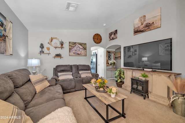 living room featuring vaulted ceiling, light carpet, and a wood stove