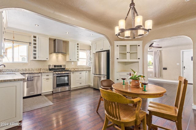 kitchen featuring dark hardwood / wood-style floors, pendant lighting, sink, stainless steel appliances, and wall chimney range hood