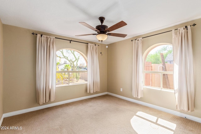 empty room featuring ceiling fan, light colored carpet, and a healthy amount of sunlight