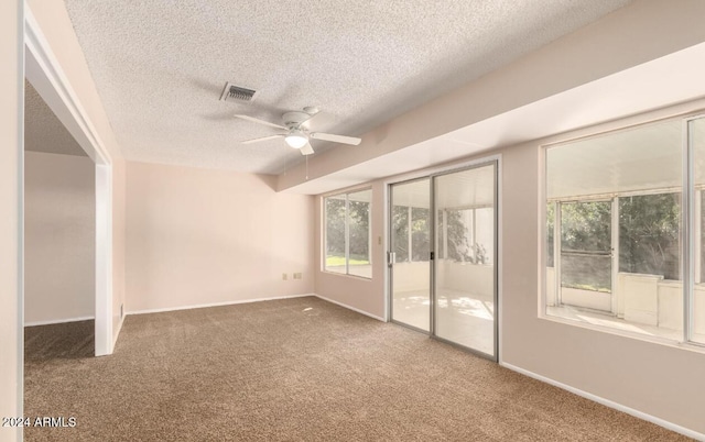 carpeted empty room with ceiling fan, plenty of natural light, and a textured ceiling