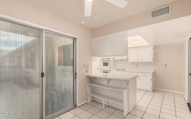 kitchen with white cabinetry, kitchen peninsula, a textured ceiling, and light tile patterned floors