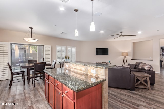 kitchen featuring dark hardwood / wood-style flooring, dark stone counters, ceiling fan, pendant lighting, and a center island